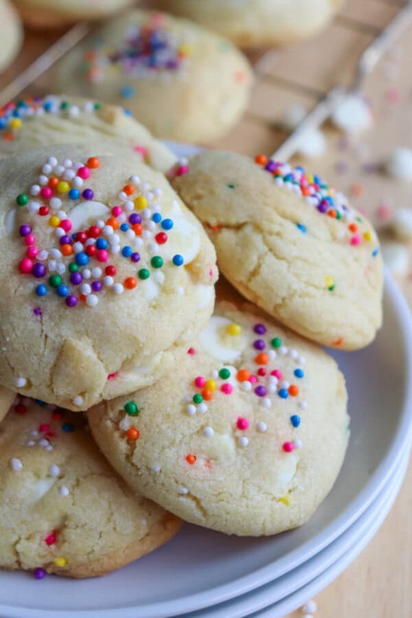 White pudding cookies with rainbow sprinkles stacked on a white plate.