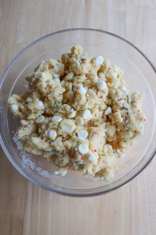 Funfetti cookie dough with white chocolate chips and rainbow sprinkles in a clear glass bowl.