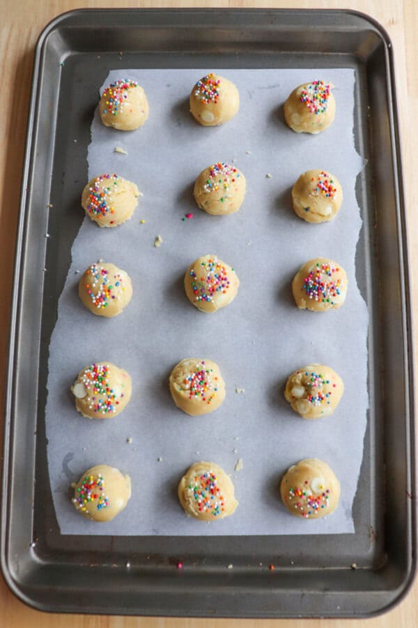 Funfetti cookie dough balls on a parchment paper lined baking sheet.