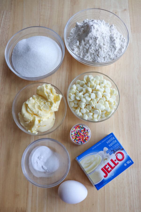 Funfetti cookie ingredients in clear glass bowls on a wooden table.