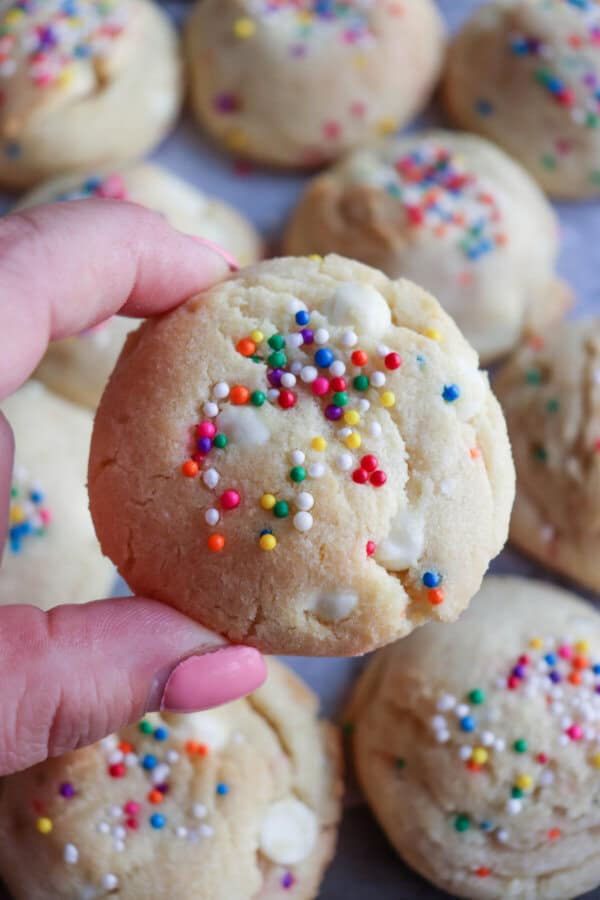 White pudding cookies with rainbow sprinkles held in a hand.
