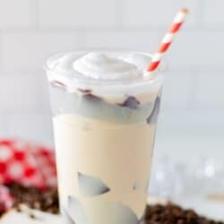 Chocolate coated plastic cup filled with coffee, topped with whipped cream and a red and white striped straw.