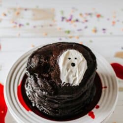 Black pancakes stacked on a white plate with a white frosting ghost on top.