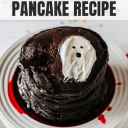 Black pancakes stacked on a white plate with a white frosting ghost on top.