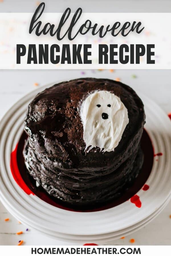 Black pancakes stacked on a white plate with a white frosting ghost on top.