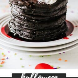 Black pancakes stacked on a white plate with a white frosting ghost on top.