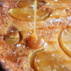 Dutch baby with apple slices and a caramel drizzle in a cast iron skillet.