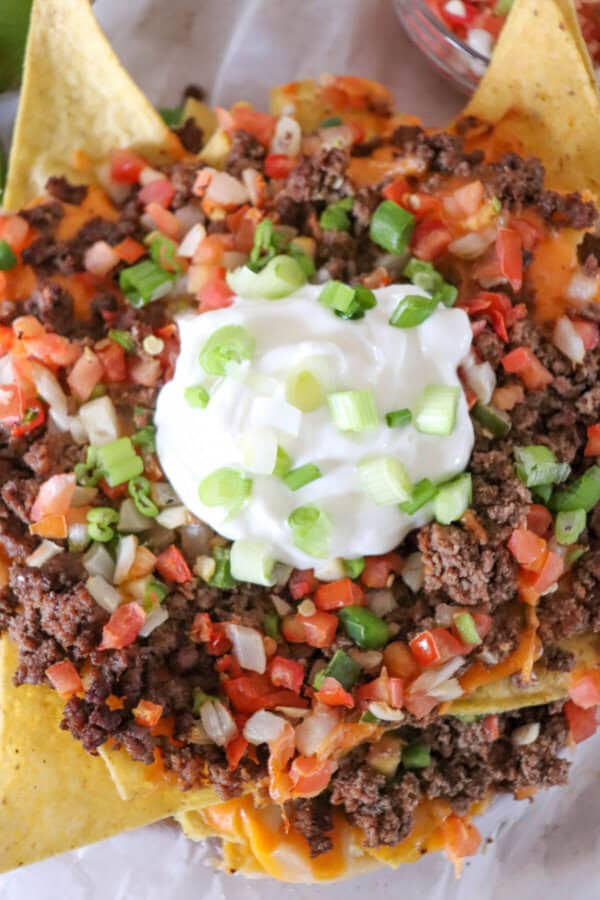 Close up of nachos with all the toppings, sour cream in the center with diced green onions.