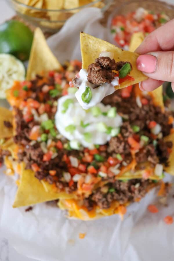 Nachos piled high with taco meat, picco, salsa and green onions with a chip taking a dip.