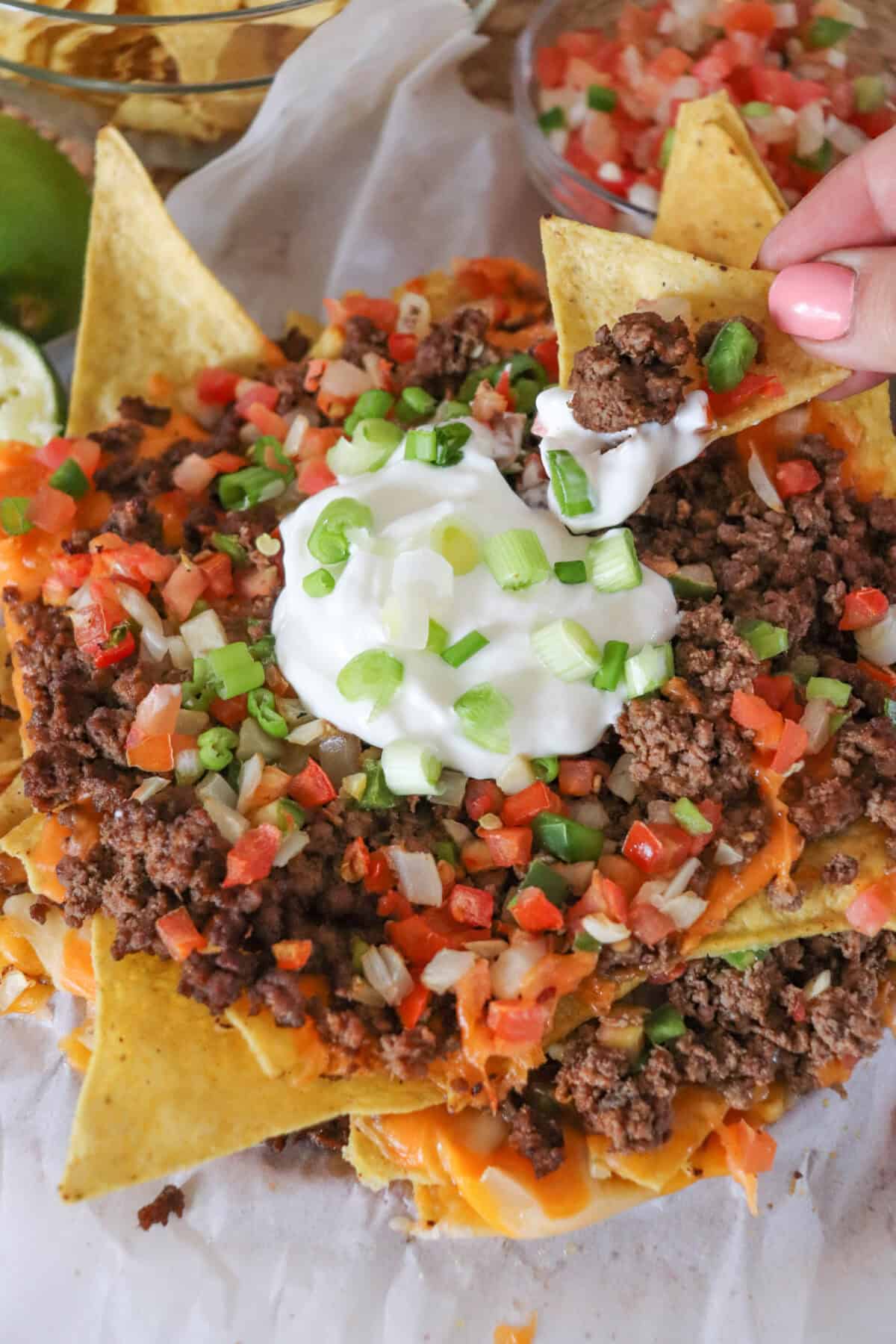 Nachos piled high with taco meat, picco, salsa and green onions with a chip taking a dip.