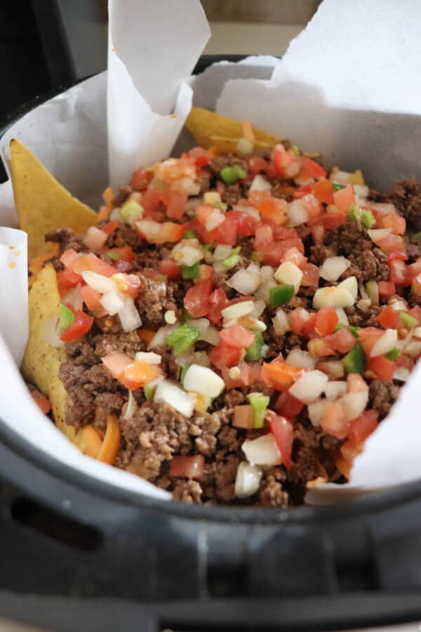 Basket of an air fryer filled with nachos and taco meat and salsa.