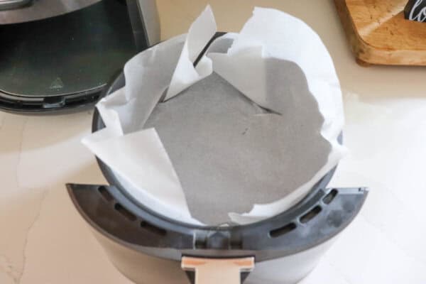 Air fryer basket lined with parchment paper.