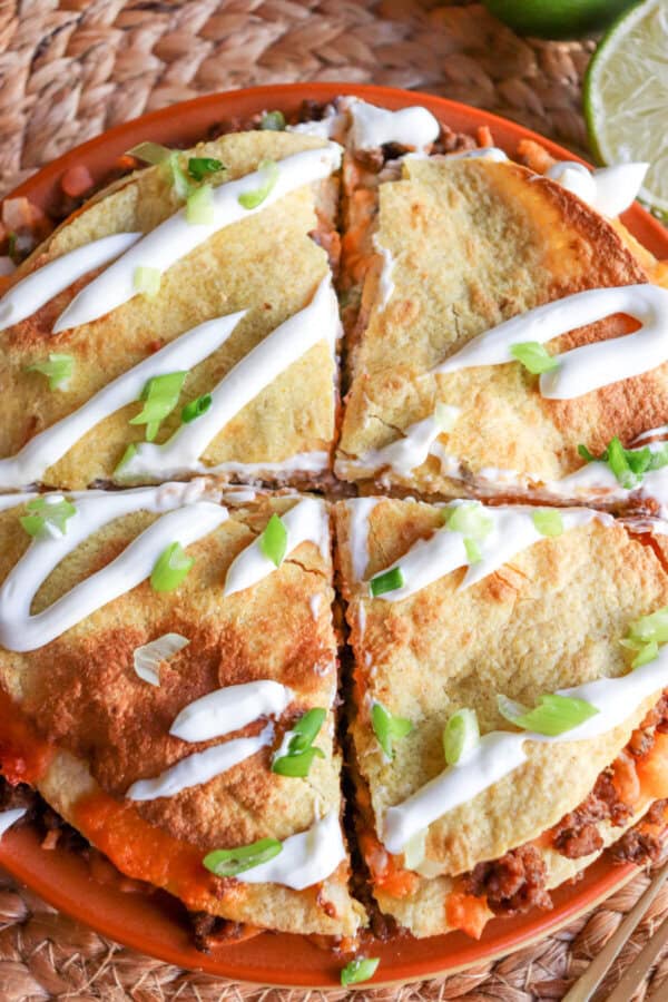 Four inch corn tortillas layered with meat and cheese and topped with lime crema and sliced green onion cut into four slices.