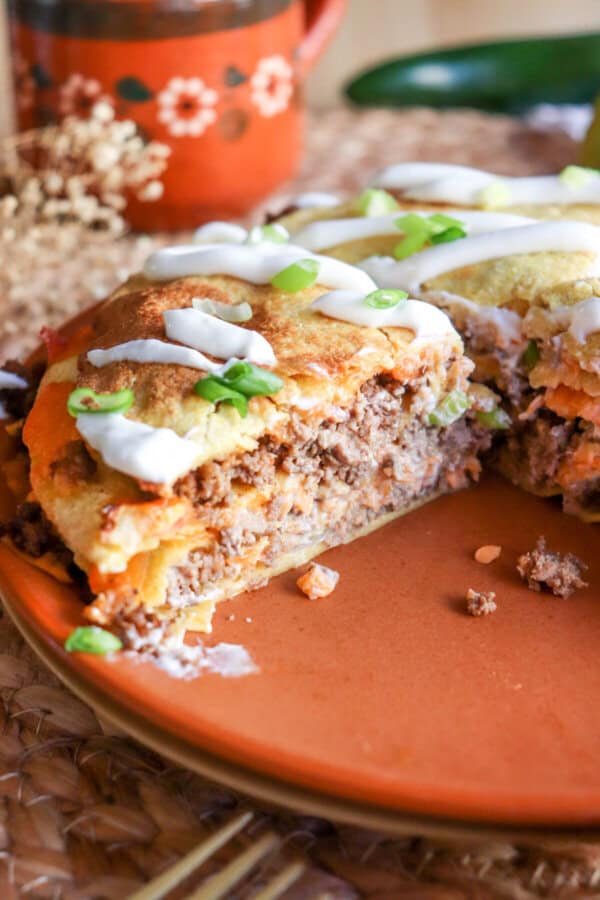 Four inch corn tortillas layered with meat and cheese and topped with lime crema and sliced green onion on an orange plate.