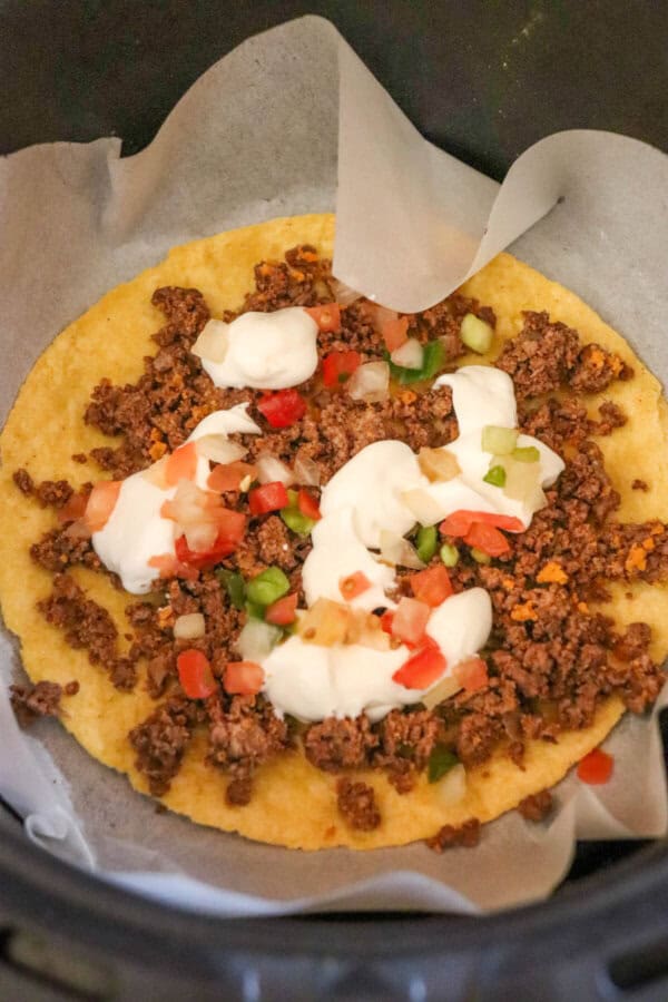 Corn tortilla in an air fryer basket with taco meat, salsa and sour cream layered on top.