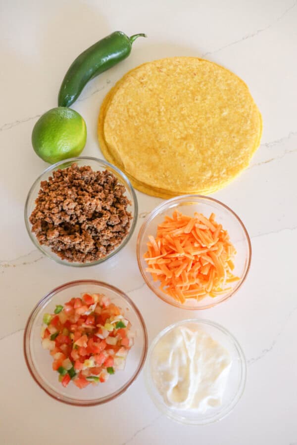 Ingredients for air fryer taco bake in clear glass bowls on a white surface.