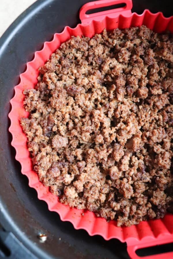 Cooked ground beef in the basket of an air fryer, lined with a red silicone basket.