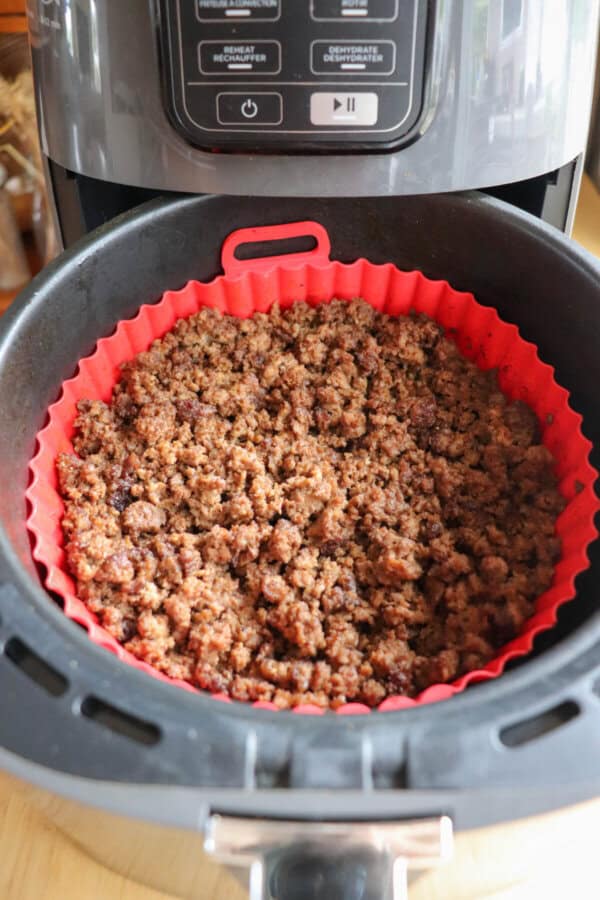 Cooked ground beef in the basket of an air fryer, lined with a red silicone basket.