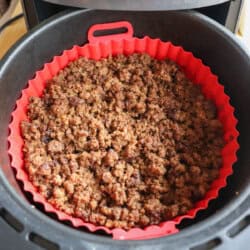 Cooked ground beef in the basket of an air fryer, lined with a red silicone basket.