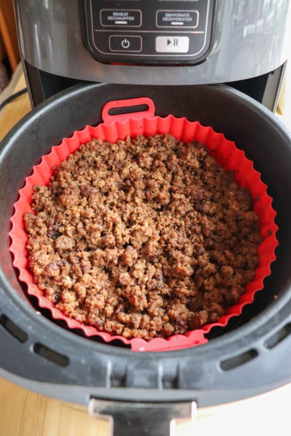 Cooked ground beef in the basket of an air fryer, lined with a red silicone basket.