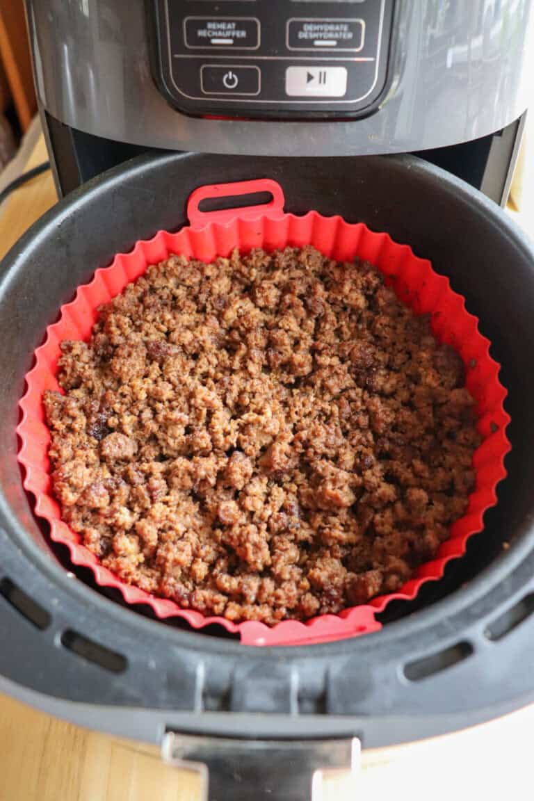 Cooked ground beef in the basket of an air fryer, lined with a red silicone basket.