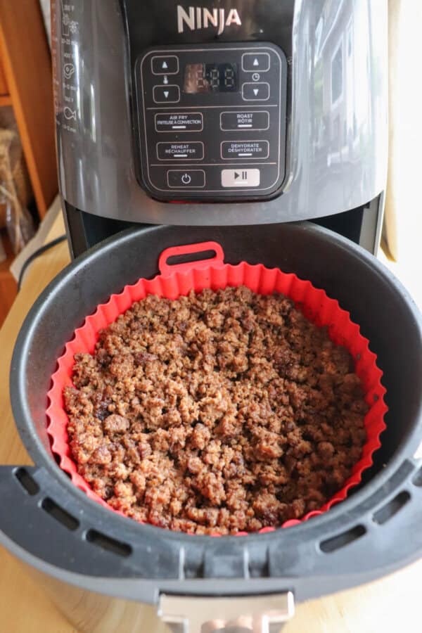 Cooked ground beef in the basket of an air fryer, lined with a red silicone basket.