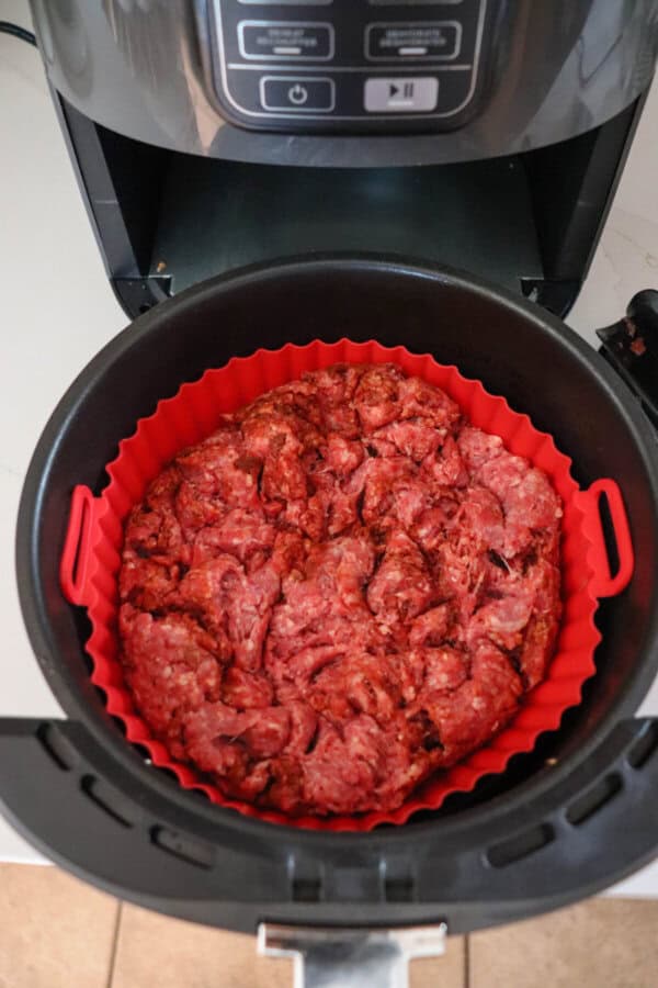 Raw taco meat in the basket of an air fryer.