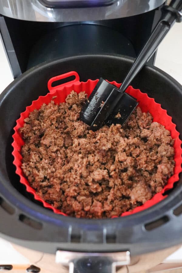 Meat masher resting in the basket of an air fryer with cooked taco meat.