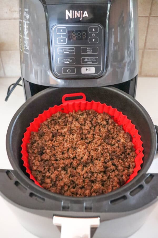 Cooked ground beef in the basket of an air fryer, lined with a red silicone basket.