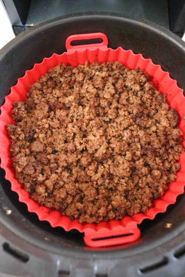 Cooked ground beef in the basket of an air fryer, lined with a red silicone basket.