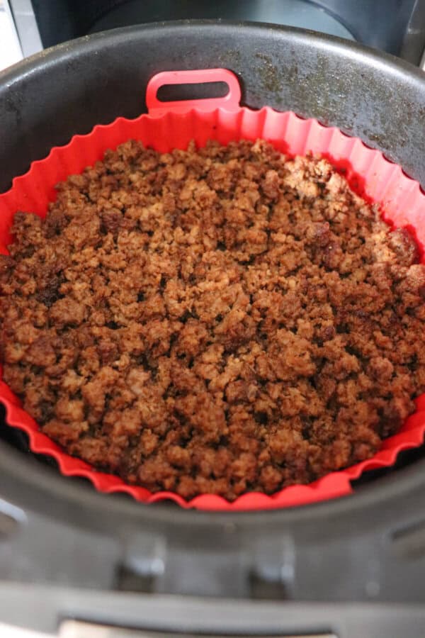 Cooked ground beef in the basket of an air fryer, lined with a red silicone basket.