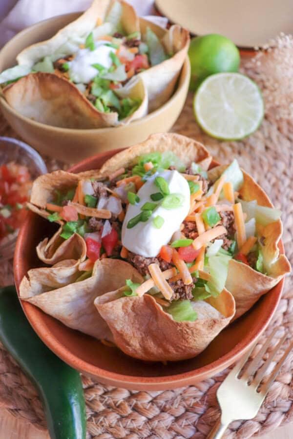 Taco salad topped with sour cream & green onions in a tortilla bowl in an orange bowl on a wooden table.