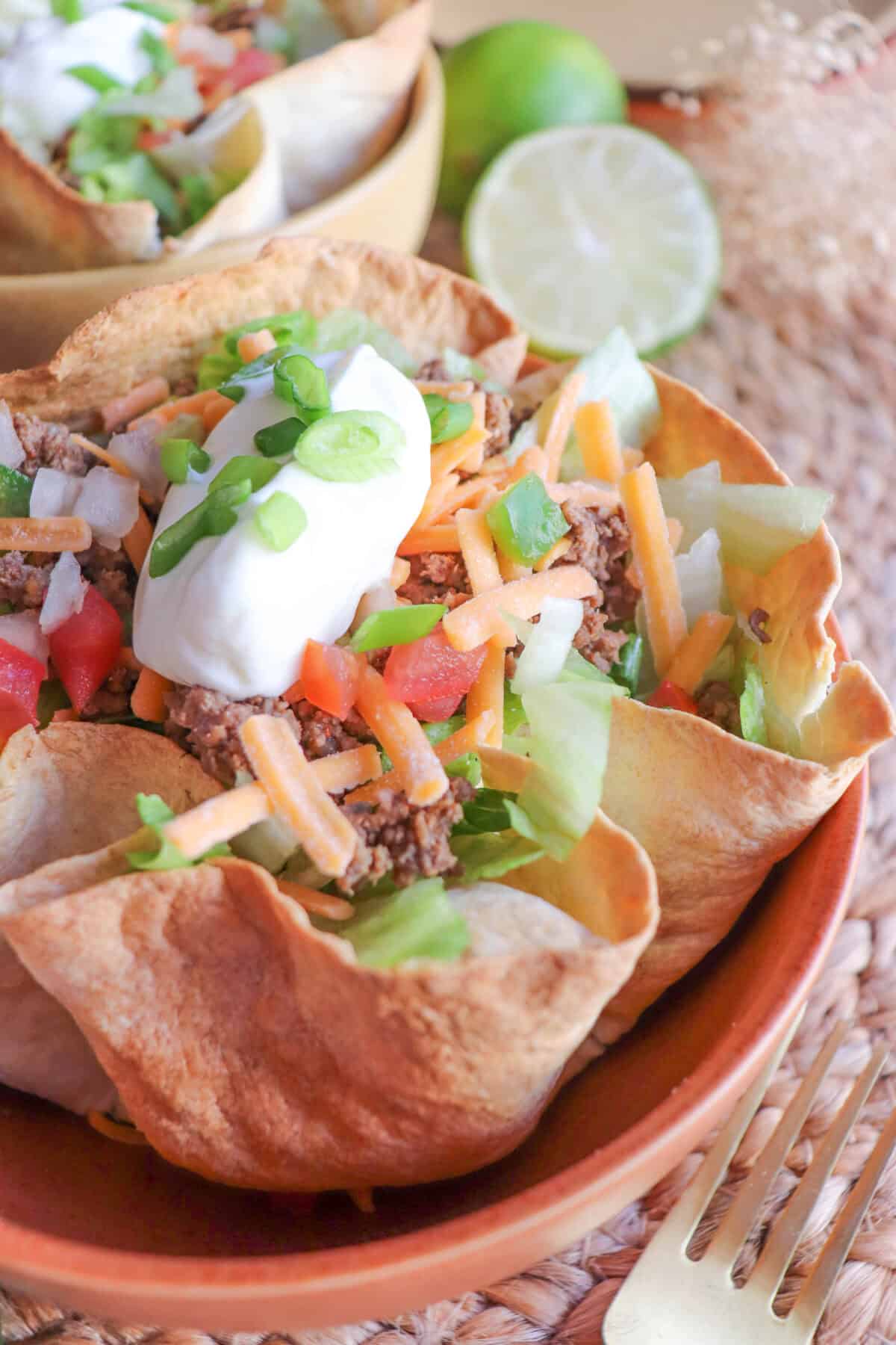 Close up of taco salad topped with sour cream & green onions in a tortilla bowl in an orange bowl.