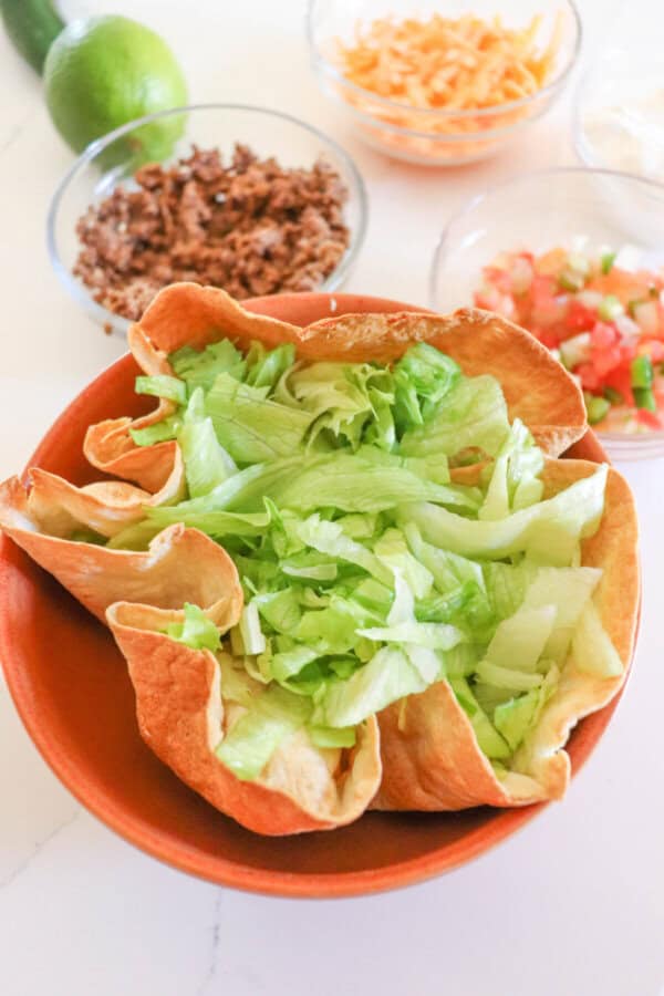 Taco bowl with shredded lettuce on an orange plate.