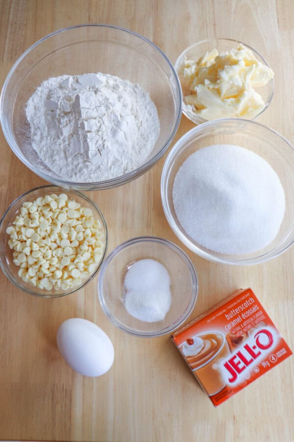 Ingredients for butterscotch pudding cookies in clear glass bowls on a wooden table.