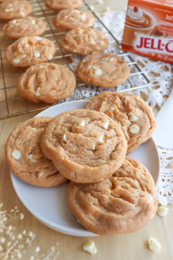 Butterscotch pudding cookies with white chocolate chips stacked on a white plate.