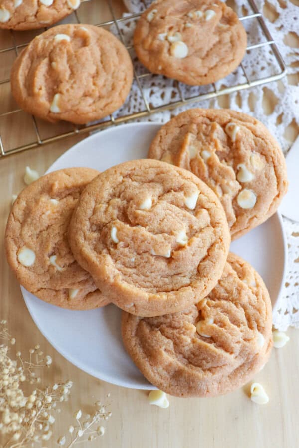 Butterscotch pudding cookies with white chocolate chips stacked on a white plate.