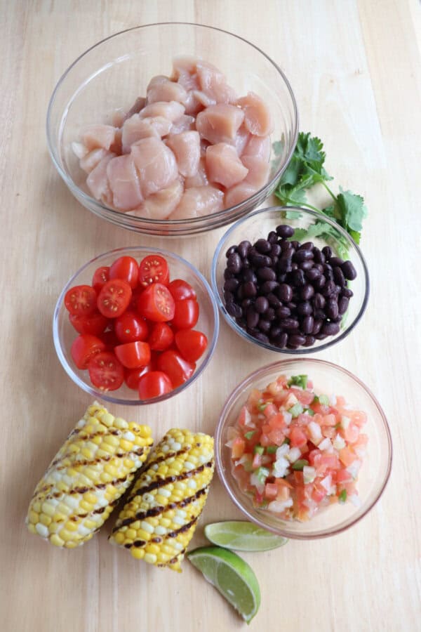 Chicken burrito bowl ingredients in clear glass bowls on a wooden table.