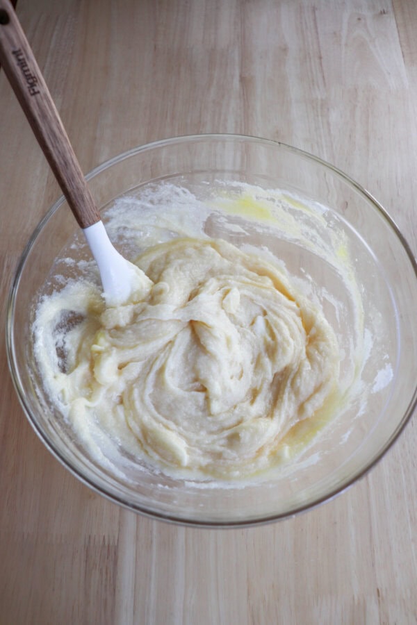 Butter and sugar creamed together in a glass mixing bowl resting on a wooden table.