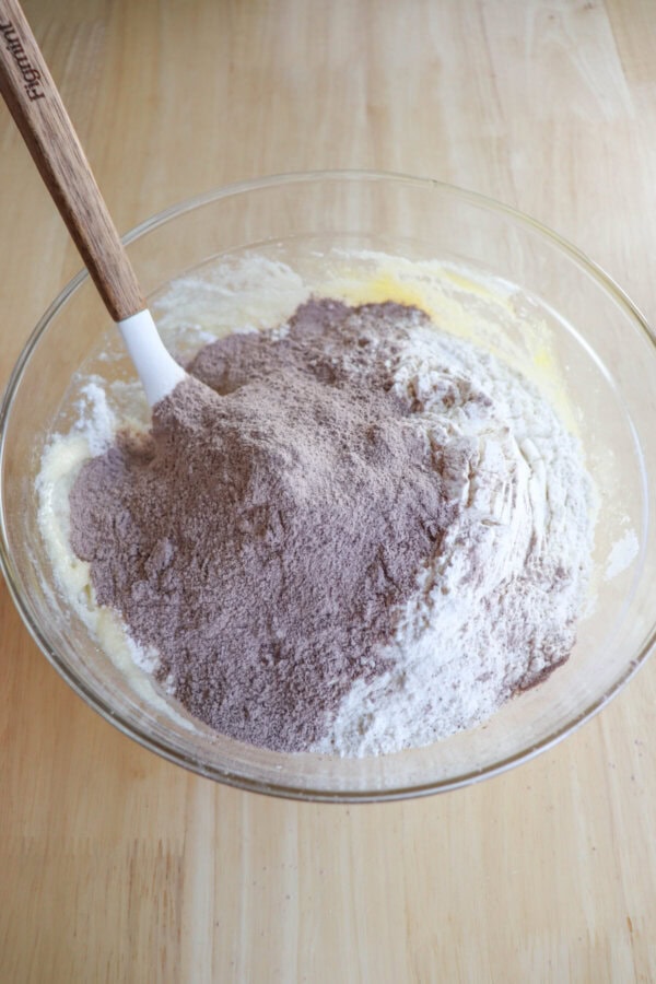 Dry chocolate pudding mix added to wet ingredients in a clear glass bowl