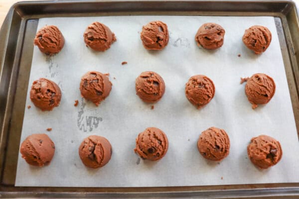 Chocolate cookie dough balls on a parchment paper lined baking sheet.