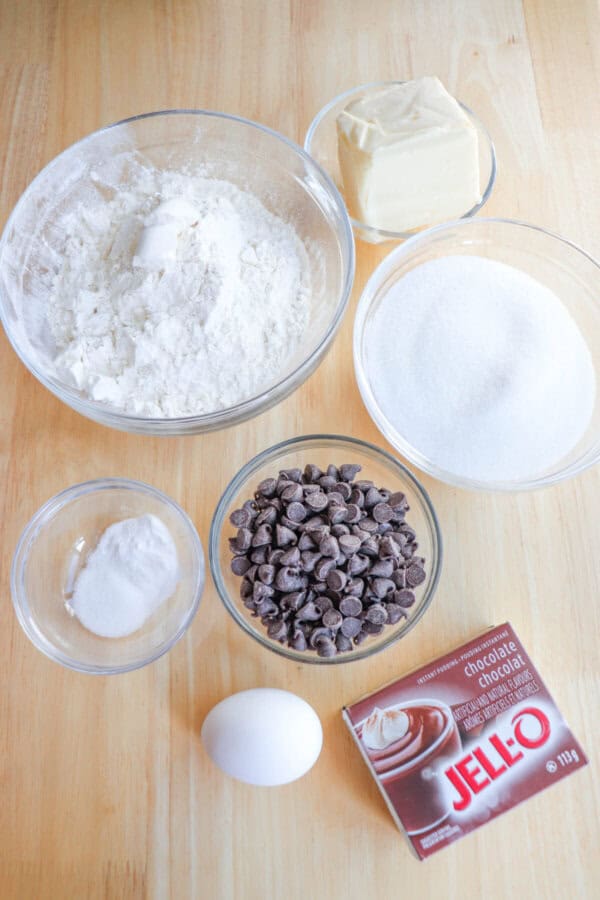 Chocolate pudding cookie ingredients in clear glass bowls on a wooden table.