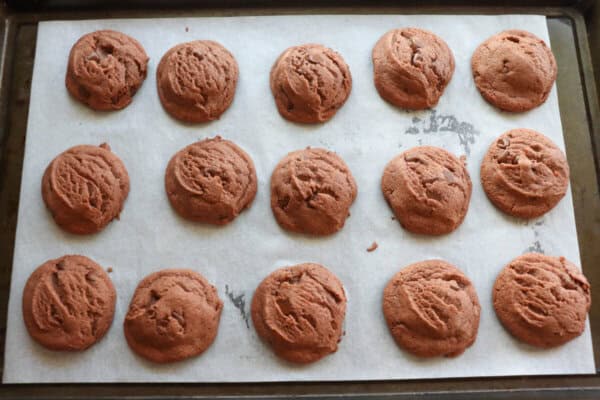 Baked chocolate cookies on a parchment paper lined baking sheet.