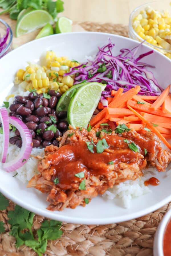 Pulled pork and vegetables over rice in a large white bowl topped with barbecue sauce.