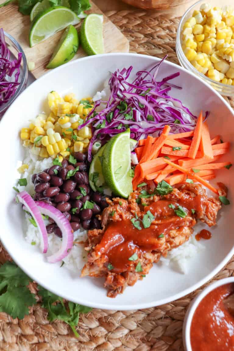 Pulled pork and vegetables over rice in a large white bowl topped with barbecue sauce.