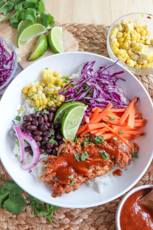 Pulled pork and vegetables over rice in a large white bowl topped with barbecue sauce.