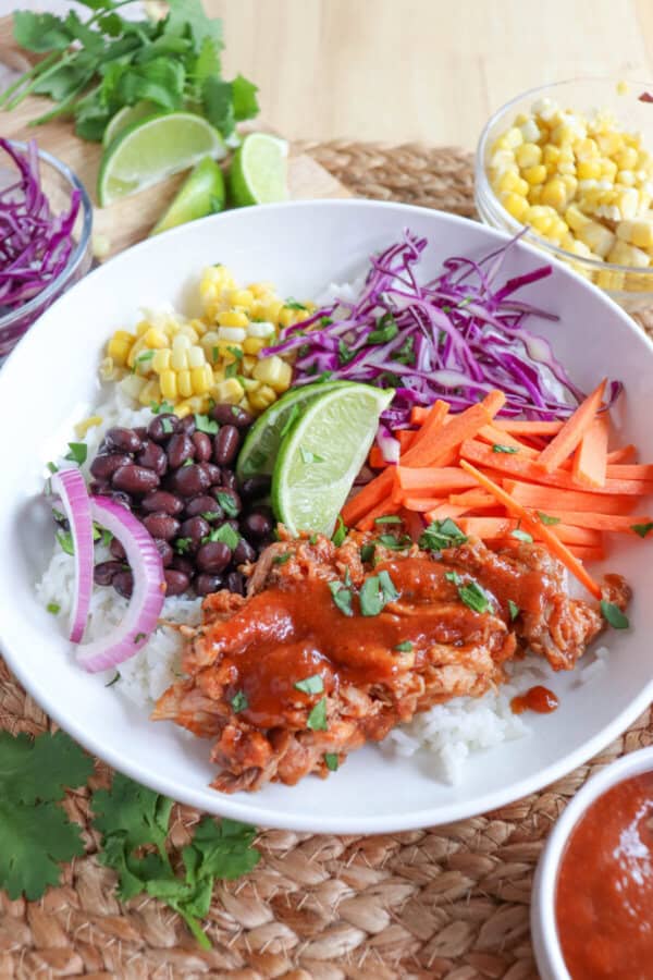 Pulled pork and vegetables over rice in a large white bowl topped with barbecue sauce.