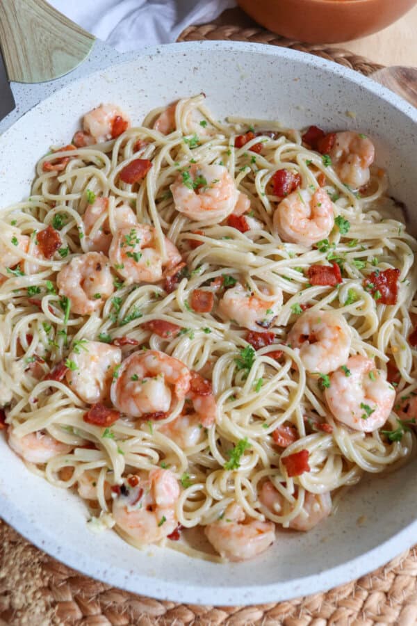 Cooked shrimp in spaghetti in a white skillet with bacon.