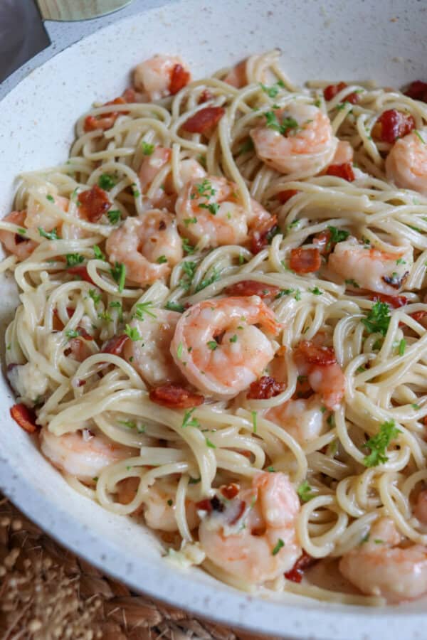 Cooked shrimp in spaghetti in a white skillet with bacon.