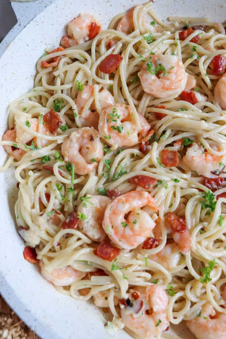 Cooked shrimp in spaghetti in a white skillet with bacon.